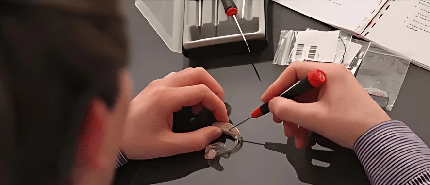 A close-up of a person holding a hearing aid, deciding between repair or replacement, with Aanvii Hearing branding in the background.